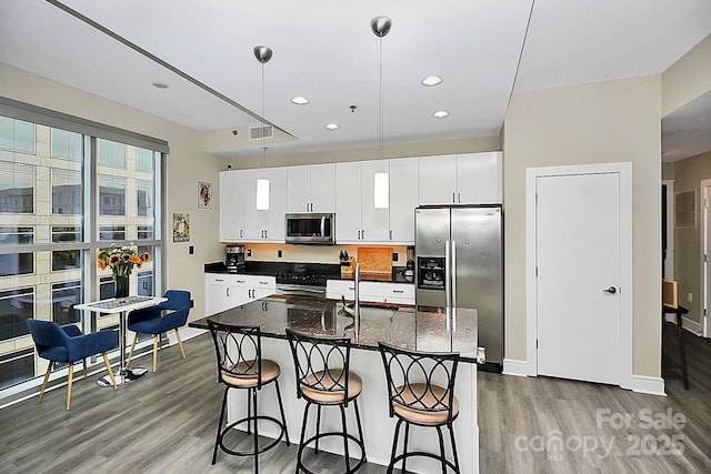 kitchen with white cabinets, a kitchen island with sink, stainless steel appliances, light wood-type flooring, and a kitchen bar
