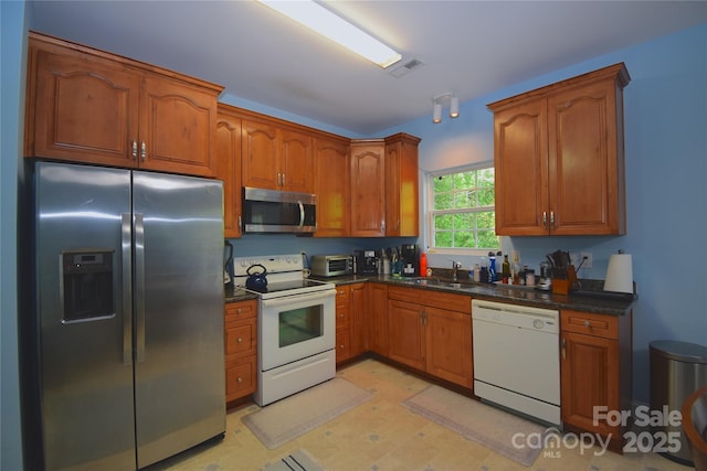 kitchen featuring brown cabinetry, appliances with stainless steel finishes, a sink, and visible vents