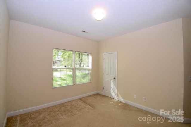 empty room featuring baseboards, visible vents, and light carpet