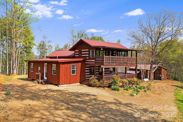 back of house featuring a wooden deck, a sunroom, dirt driveway, and metal roof