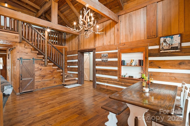 dining room featuring beam ceiling, an inviting chandelier, wood walls, stairs, and wooden ceiling