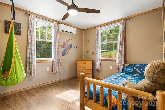 bedroom featuring a wall mounted AC, wood finished floors, baseboards, and multiple windows