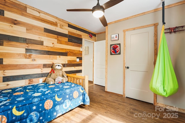 bedroom with wooden walls, wood finished floors, and a ceiling fan