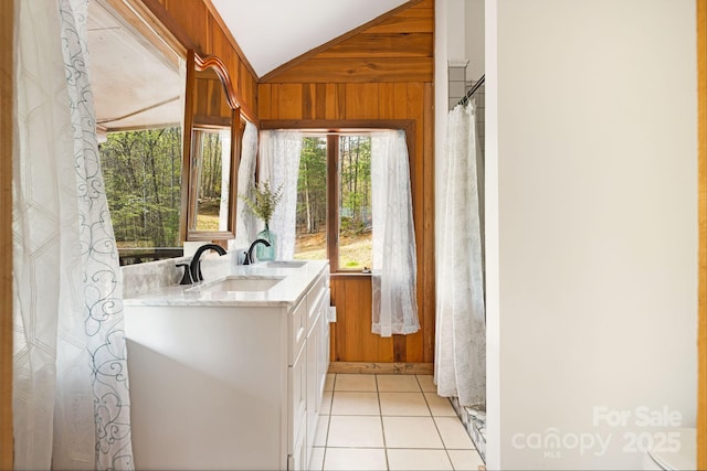 interior space with vaulted ceiling, a sink, double vanity, wood walls, and tile patterned flooring