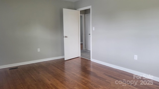 empty room featuring wood finished floors, visible vents, and baseboards