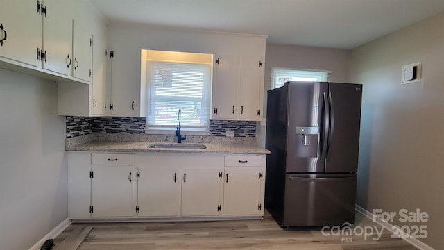 kitchen featuring stainless steel fridge, a sink, white cabinets, and plenty of natural light