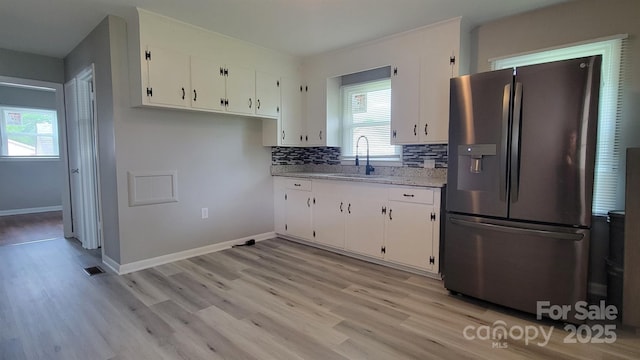 kitchen featuring stainless steel refrigerator with ice dispenser, light wood finished floors, white cabinets, and a sink