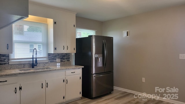 kitchen with tasteful backsplash, stainless steel fridge, a sink, white cabinetry, and light wood-type flooring