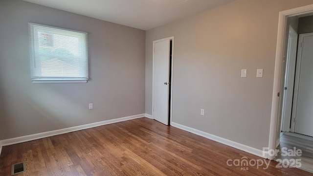 unfurnished bedroom with baseboards, visible vents, wood finished floors, and a closet
