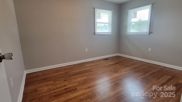 empty room featuring baseboards and dark wood-type flooring
