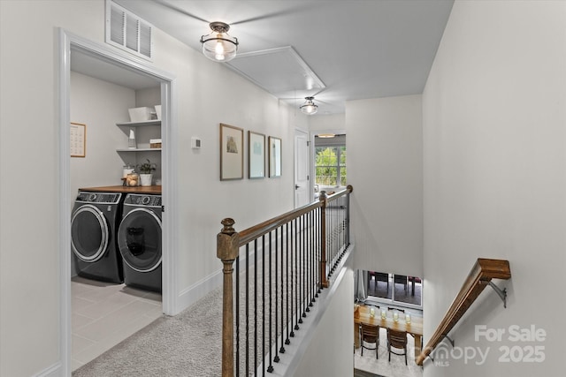 hallway with an upstairs landing, visible vents, attic access, washer and clothes dryer, and tile patterned floors