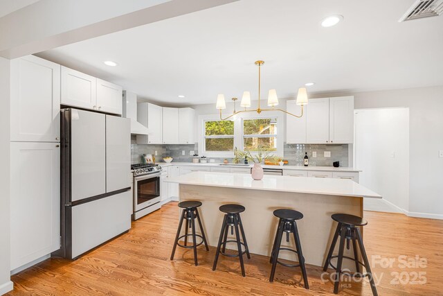 16 Graystone Rd, Asheville, NC 28804 - kitchen featuring a breakfast bar, stainless steel gas stove, light countertops, wall chimney exhaust hood, and freestanding refrigerator