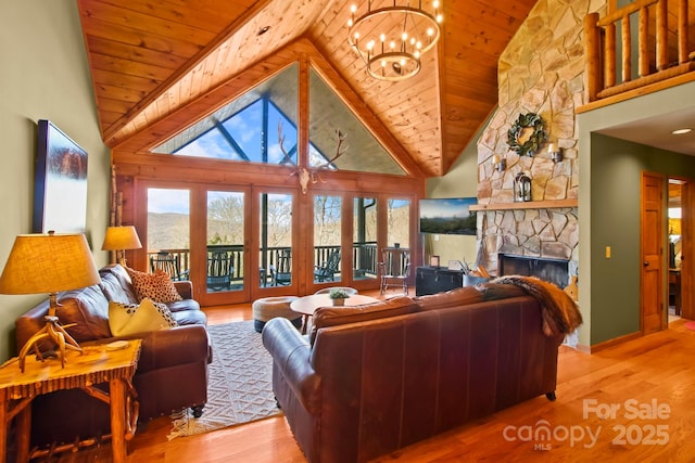 living area with wood finished floors, a stone fireplace, wooden ceiling, a chandelier, and high vaulted ceiling