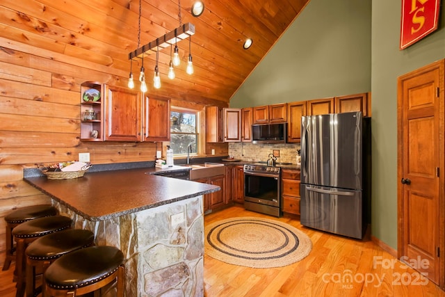 kitchen with dark countertops, a peninsula, appliances with stainless steel finishes, and light wood-style flooring