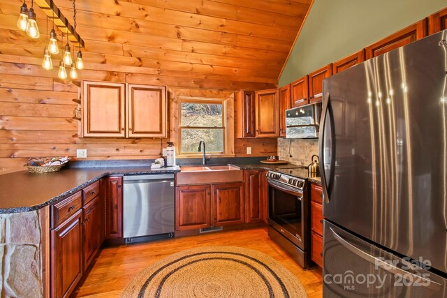 kitchen featuring stainless steel appliances, a sink, dark countertops, vaulted ceiling, and light wood-style floors