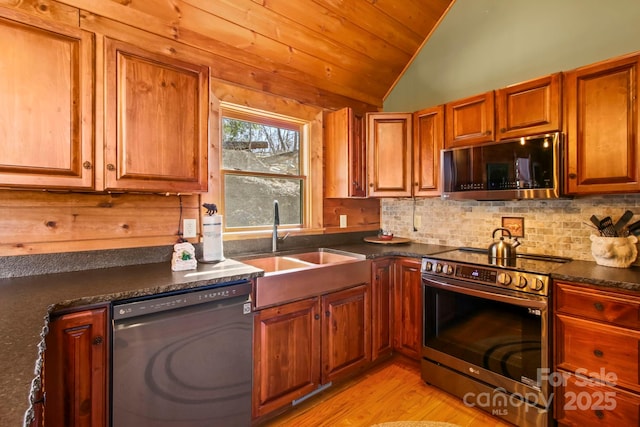 kitchen with stainless steel appliances, dark countertops, vaulted ceiling, a sink, and decorative backsplash