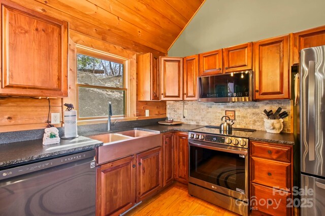 kitchen with stainless steel appliances, dark countertops, vaulted ceiling, a sink, and decorative backsplash