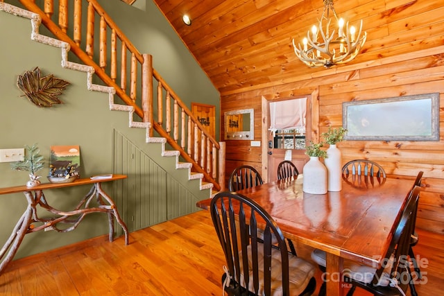 dining area featuring stairs, wood finished floors, wooden walls, wooden ceiling, and a notable chandelier