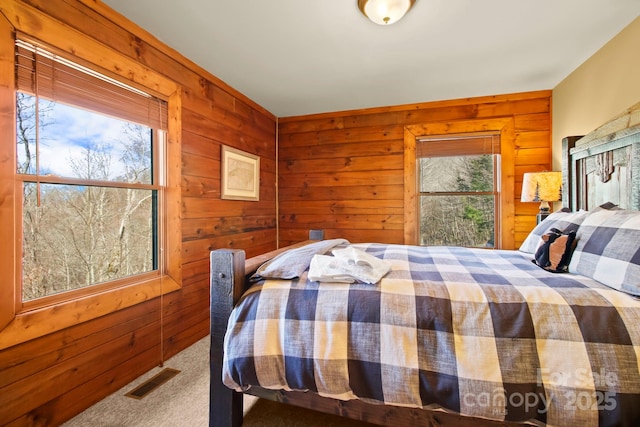 carpeted bedroom featuring wooden walls and visible vents