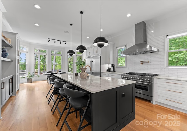 3933 Ayrshire Pl, Charlotte, NC 28210 - kitchen with decorative backsplash, a kitchen island with sink, white cabinetry, premium appliances, and wall chimney exhaust hood