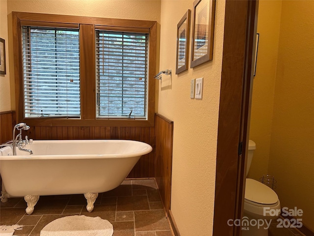 222 Creekside Way, Burnsville, NC 28714 - bathroom featuring a soaking tub, a textured wall, stone tile flooring, and a wainscoted wall
