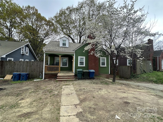 view of front of home featuring fence, covered porch, and roof with shingles