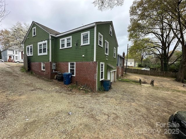 view of side of property with dirt driveway, brick siding, fence, and a garage