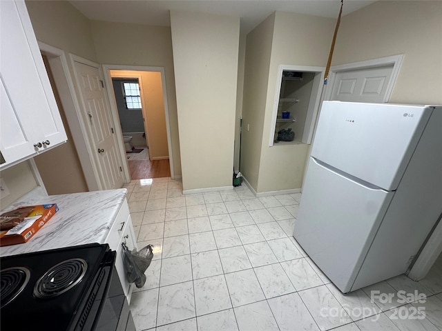 kitchen featuring freestanding refrigerator, black range with electric cooktop, marble finish floor, light countertops, and white cabinets