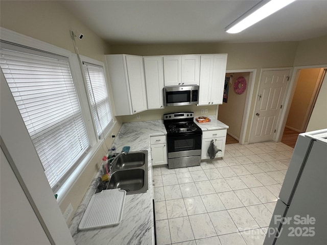 kitchen with light stone counters, a sink, white cabinetry, and stainless steel appliances