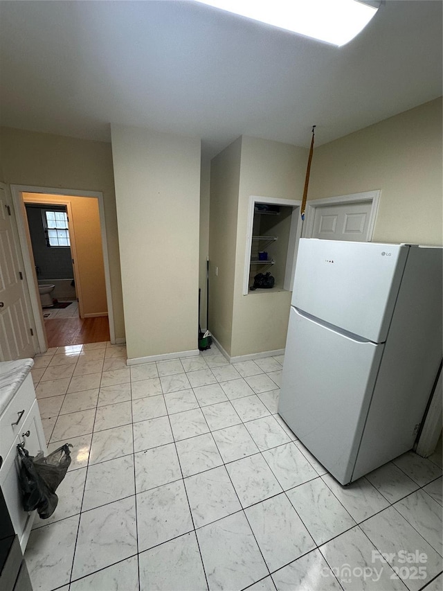 kitchen with freestanding refrigerator, marble finish floor, white cabinetry, and light countertops