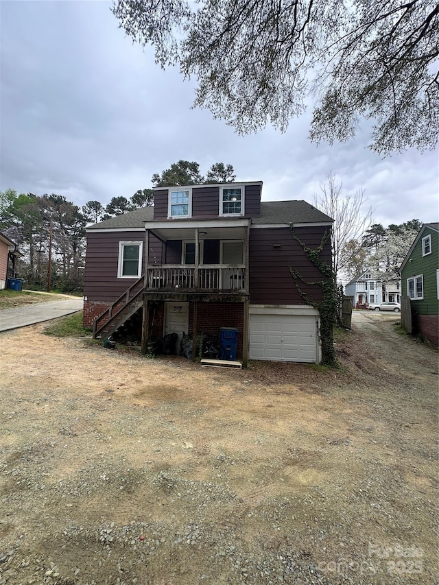 view of front of property with stairway, covered porch, dirt driveway, and a garage