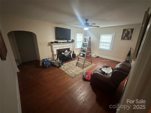 living area featuring arched walkways, ceiling fan, a tiled fireplace, and wood finished floors