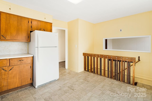 kitchen featuring brown cabinetry, stone finish floor, light countertops, and freestanding refrigerator