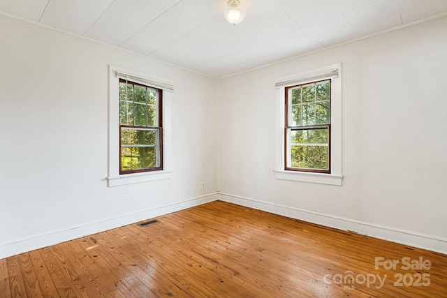 unfurnished room with baseboards, hardwood / wood-style floors, visible vents, and a wealth of natural light
