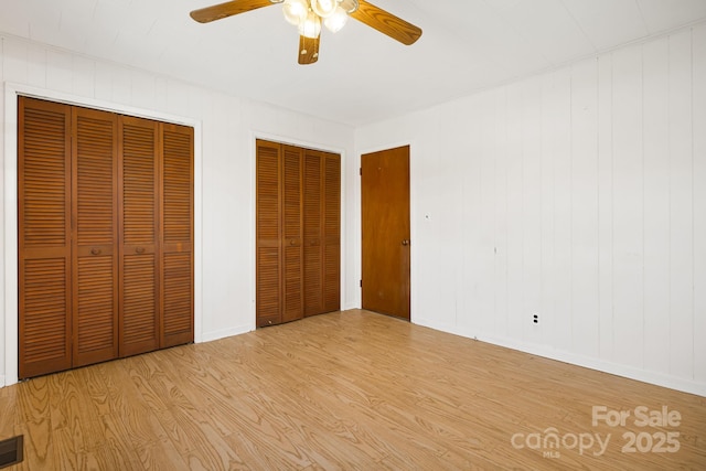 unfurnished bedroom with light wood-type flooring, baseboards, visible vents, ceiling fan, and multiple closets