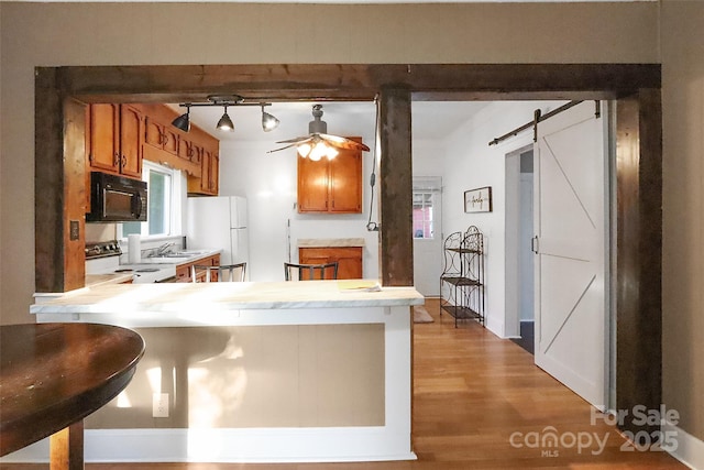 kitchen featuring a barn door, brown cabinets, white appliances, light wood finished floors, and light countertops