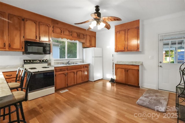 kitchen featuring a sink, brown cabinets, white appliances, light wood finished floors, and light countertops