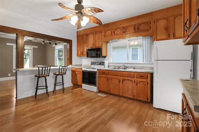 kitchen with a sink, brown cabinets, white appliances, ceiling fan, and light countertops