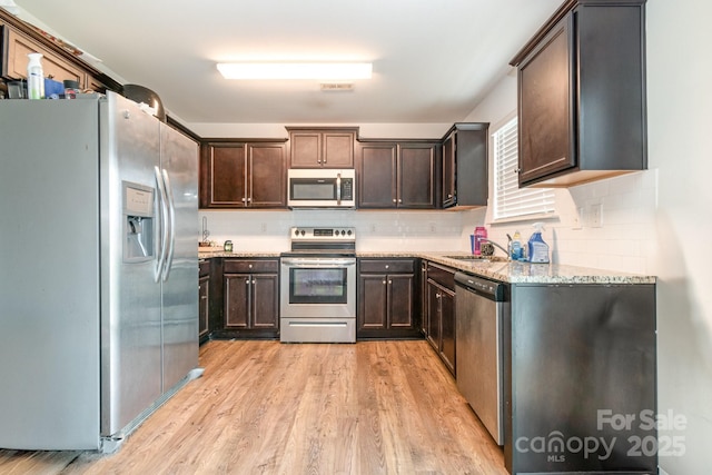 3033 Green Apple Dr, Dallas, NC 28034 - kitchen featuring light stone countertops, decorative backsplash, appliances with stainless steel finishes, dark brown cabinets, and light wood-type flooring