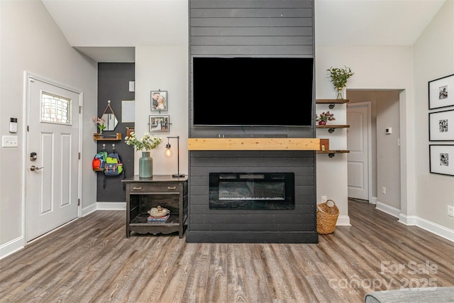 living area with baseboards, wood finished floors, and a glass covered fireplace