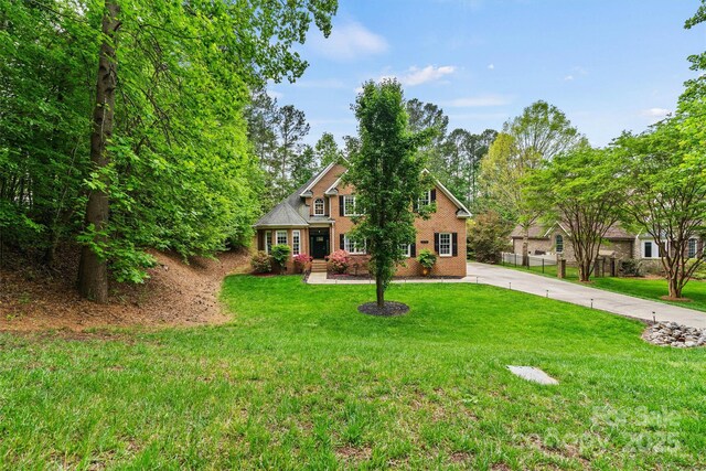 traditional-style house featuring brick siding, a front yard, and concrete driveway