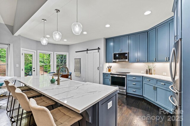 kitchen with a barn door, blue cabinets, appliances with stainless steel finishes, dark wood-style floors, and recessed lighting