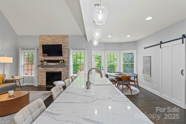 dining area featuring a barn door, dark wood-style flooring, a tile fireplace, and a healthy amount of sunlight