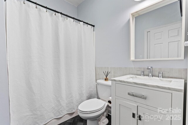 bathroom featuring a wainscoted wall, toilet, tile walls, shower / bath combination with curtain, and vanity