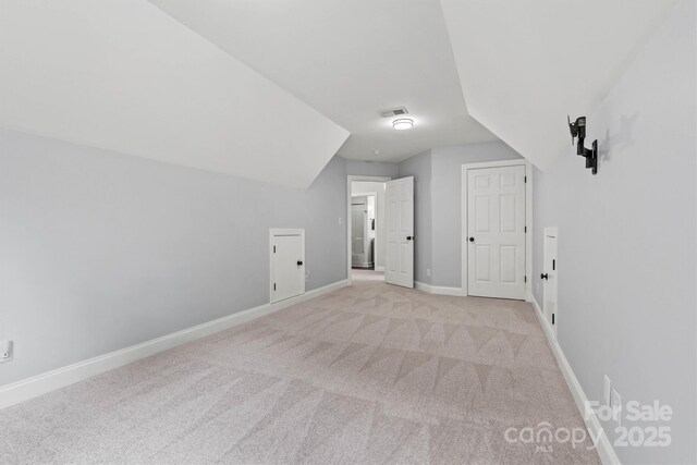 additional living space featuring light carpet, lofted ceiling, and baseboards