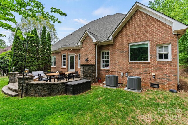 rear view of property with central air condition unit, brick siding, a yard, and a patio
