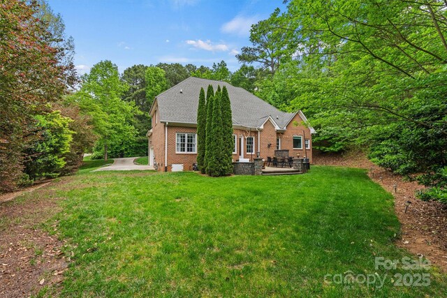 back of house with a lawn, a shingled roof, brick siding, and a patio