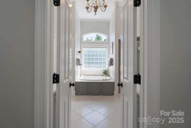 full bathroom with an inviting chandelier, ornamental molding, a garden tub, and tile patterned flooring