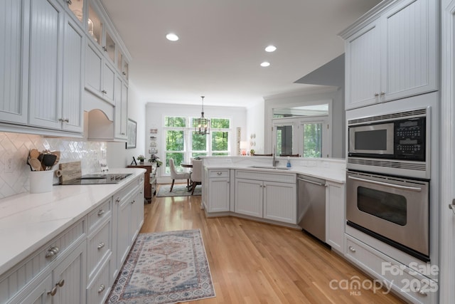 kitchen featuring a sink, light wood-style floors, stainless steel appliances, a peninsula, and decorative backsplash