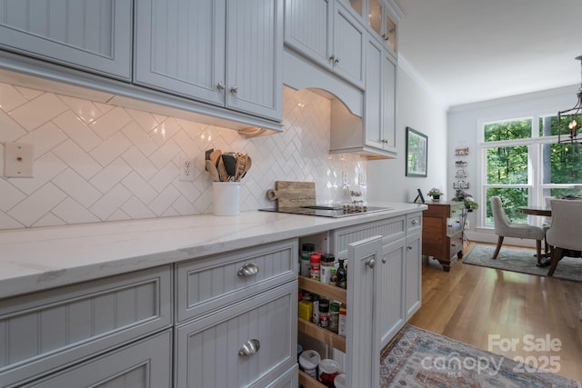 kitchen featuring crown molding, glass insert cabinets, tasteful backsplash, light stone counters, and light wood finished floors